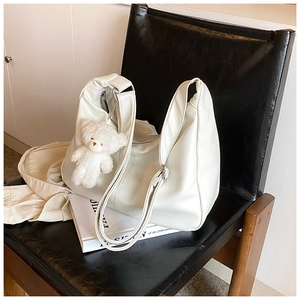 Gros plan du sac cabas blanc en cuir avec porte-clés ours sur un siège noir chic