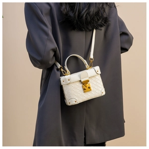 Close-up of white woven box bucket bag with gold hardware worn over grey blazer