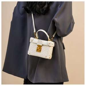 Close-up of white woven leather bucket bag with gold hardware on a grey blazer suit