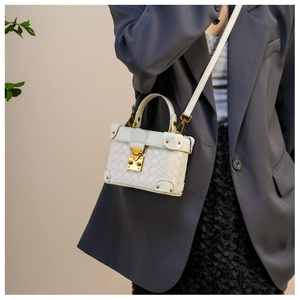 Close-up of white woven box bucket bag featuring gold metal locks and elegant texture