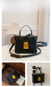Close-up of black box-shaped bag with woven texture, gold metal lock, and reinforced corners