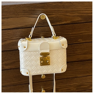 Detail of white woven bucket bag with gold lock and metal corner rivets on wood background