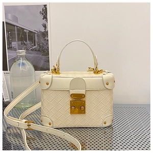 Close-up of white woven bucket bag with gold metal clasp and adjustable shoulder strap