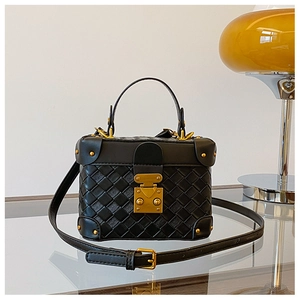 Detail of black woven leather bucket bag featuring gold metal clasp and top handle