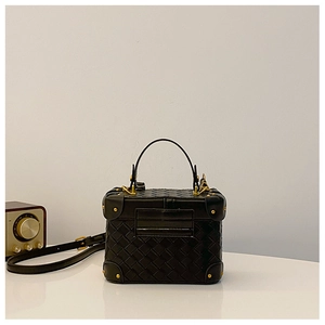 Close-up of black woven leather bucket bag with gold rivets and metallic lock hardware