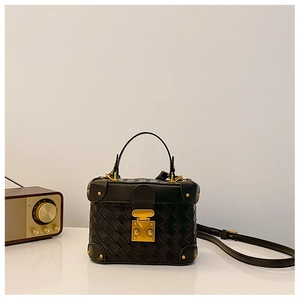 Detail of black woven texture handbag with gold metal clasp and adjustable shoulder strap