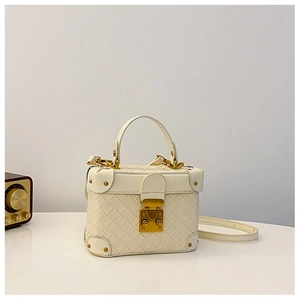 Detail of cream woven bucket bag showing the metal clasp and protective riveted corners