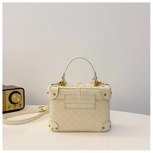 Detail view of cream woven bucket bag with gold studs and adjustable shoulder strap