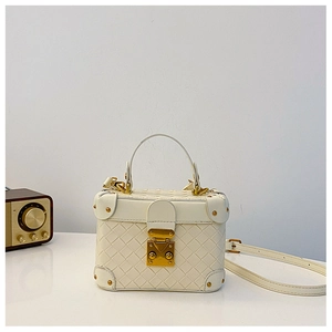Detail view of woven leather texture and gold metal clasp on a cream white bucket bag