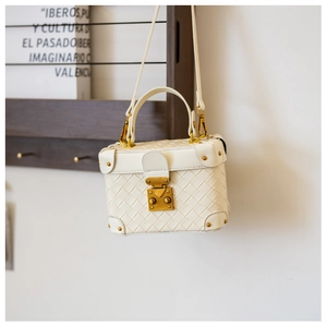 Detailed close-up of a white woven box bag with gold metal buckle and studs
