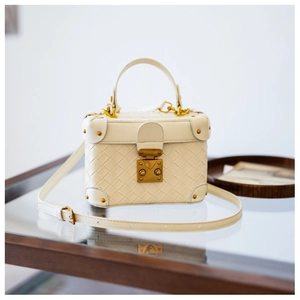 Detailed view of white woven leather bucket bag with gold lock and adjustable strap