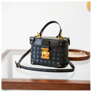 Detail of black woven leather box bag with gold metal lock on a glass table