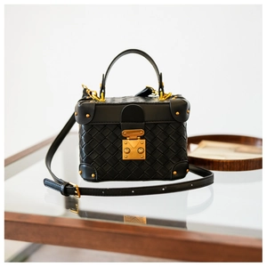 Close-up of woven leather texture with gold metal buckle and studs on a black bucket bag