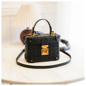 Detailed macro view of black woven box bag with vintage gold hardware on marble surface