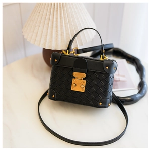 Detailed macro view of black woven leather mini trunk bag with gold metallic buckles