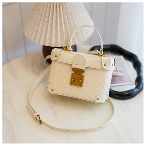 Detail of white woven bucket bag with vintage bronze hardware on a marble surface