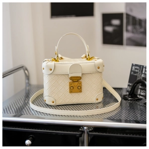 Close-up of white woven leather bucket bag featuring gold metal lock and vintage trunk style