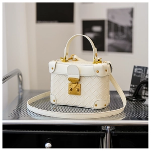 Close-up of white woven bucket bag with gold clasp and rivet reinforced corners