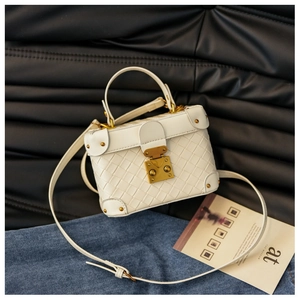 Detailed view of woven cream bucket bag with vintage gold S-lock and metal corner accents