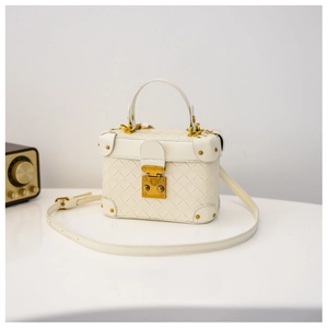 Detail of white woven box bag with gold metal clasp and rivets on a white surface