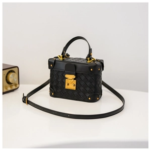 Close-up of black woven texture and polished gold metal lock on the stylish box handbag
