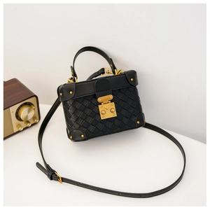 Detail of a black woven mini box bag with gold metal latches and vintage rivets