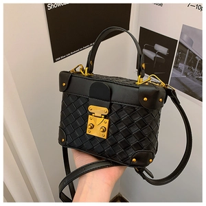 Detail of black woven mini box bag with gold lock and rivets on a minimalist background