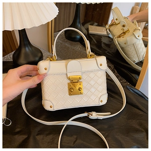 Close-up of a white woven texture handbag with golden metal lock and rivet details