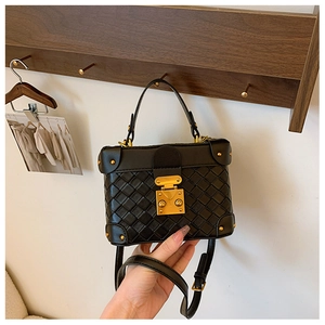 Detail of black woven texture leather box bag with gold rivet lock and metal corners