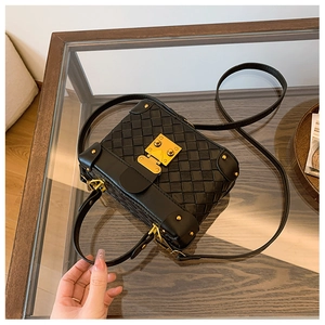 Macro view of woven black leather bucket bag featuring gold-tone lock and corner studs