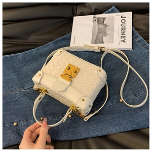 Top-down view of white woven bucket bag with vintage gold clasp on denim texture
