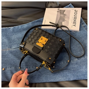 Detail of black woven leather box bag featuring golden metal lock and textured handle
