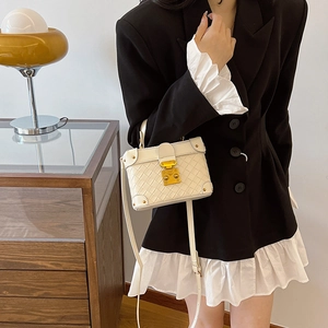 Chic white quilted box bucket bag with gold clasp shown on a model in a black suit