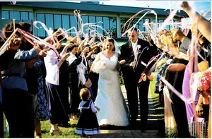 Guests waving pink silk ribbon wands for wedding couple entrance in outdoor party