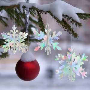 Close-up of 3D iridescent snowflake ornaments hanging on snowy pine branches