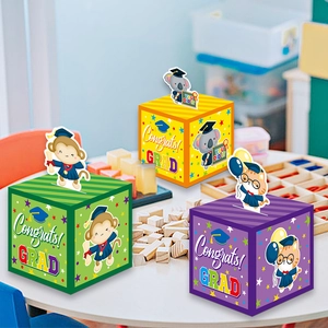 Three colorful graduation gift boxes with cartoon animal toppers on wooden desk
