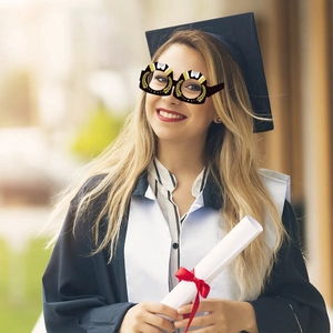 Smiling graduate in gown wearing black and gold paper glasses with laurel leaf pattern