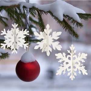 3D white paper snowflake ornaments and red Christmas ball hanging on a snowy pine branch