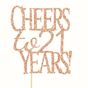 Detail of rose gold glitter cake topper featuring Cheers to 21 Years text with wooden stick