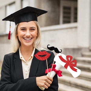 Smiling graduate in gown holding glittery lips and mustache photo booth props for ceremony