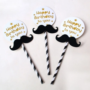 Close-up of birthday cake toppers with black mustache design and Happy Birthday gold text