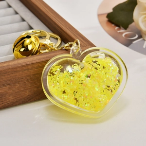 Detail of yellow glitter heart keychain with golden bell on a dark wood box