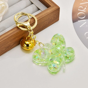 Close-up of green butterfly keychain with glitter sequins and gold bell detail