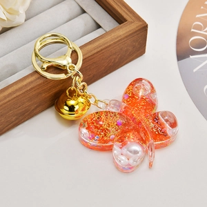Close-up of orange butterfly liquid keychain with gold sequins and pearls decoration