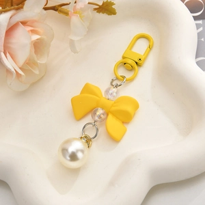 Detail of yellow bow keychain with large pearl pendant and colorful beads on tray