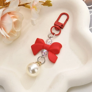 Detail of red bow keychain with pearl and translucent beads on a white cloud tray