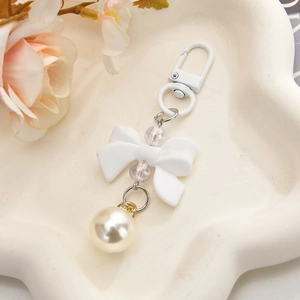Detail of white matte bow keychain with iridescent beads and pearl pendant on a tray