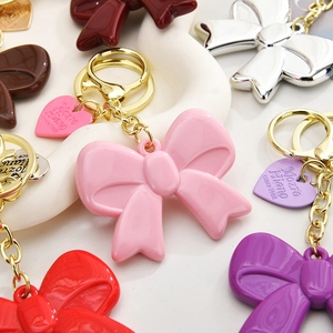 Close-up of colorful acrylic bow keychains with gold metal rings on a white plate