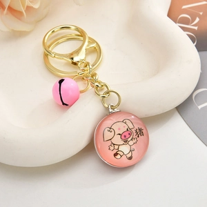 Close-up of pink 3D pig keychain with golden bell and ring on a ceramic tray