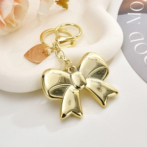 Exquisite golden acrylic bow keychain with lobster clasp and heart tag on a white tray
